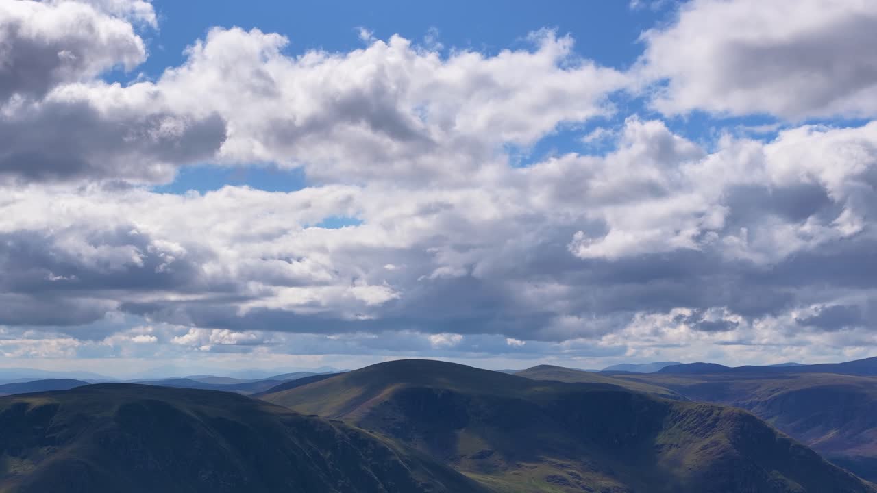 Drone camera glides above tranquil Scottish Highlands, revealing rolling hills, heather, and dramatic clouds