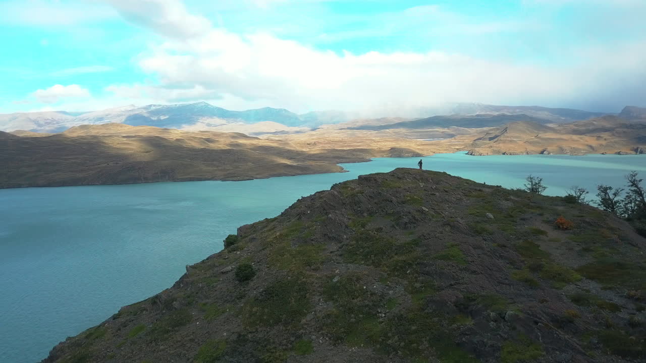 vista aérea de un dron de un excursionista de pie en la cima de una montaña mirando un lago pintoresco en la patagonia
