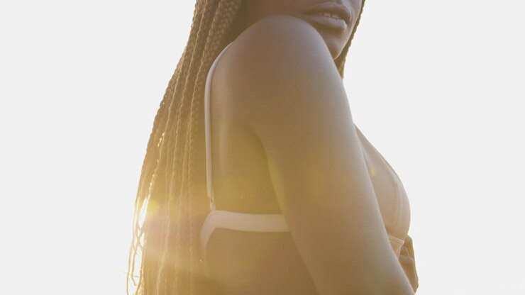 Modella africana in costume da bagno sorride mentre posa in bikini su una spiaggia