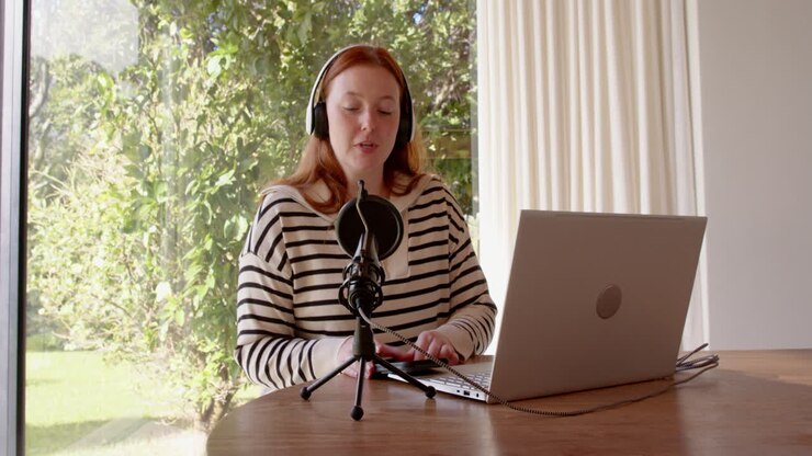 Recording podcast, woman using laptop and microphone, wearing headphones indoors