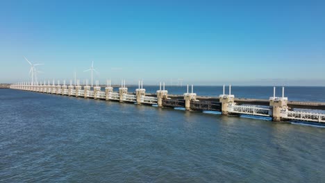 Toma-Aérea-En-Cámara-Lenta-De-La-Barrera-Contra-La-Marejada-Ciclónica-Del-Este-De-Scheldt-Y-Turbinas-Eólicas-En-La-Distancia-En-Zelanda,-Los-Países-Bajos-En-Un-Hermoso-Día-Soleado