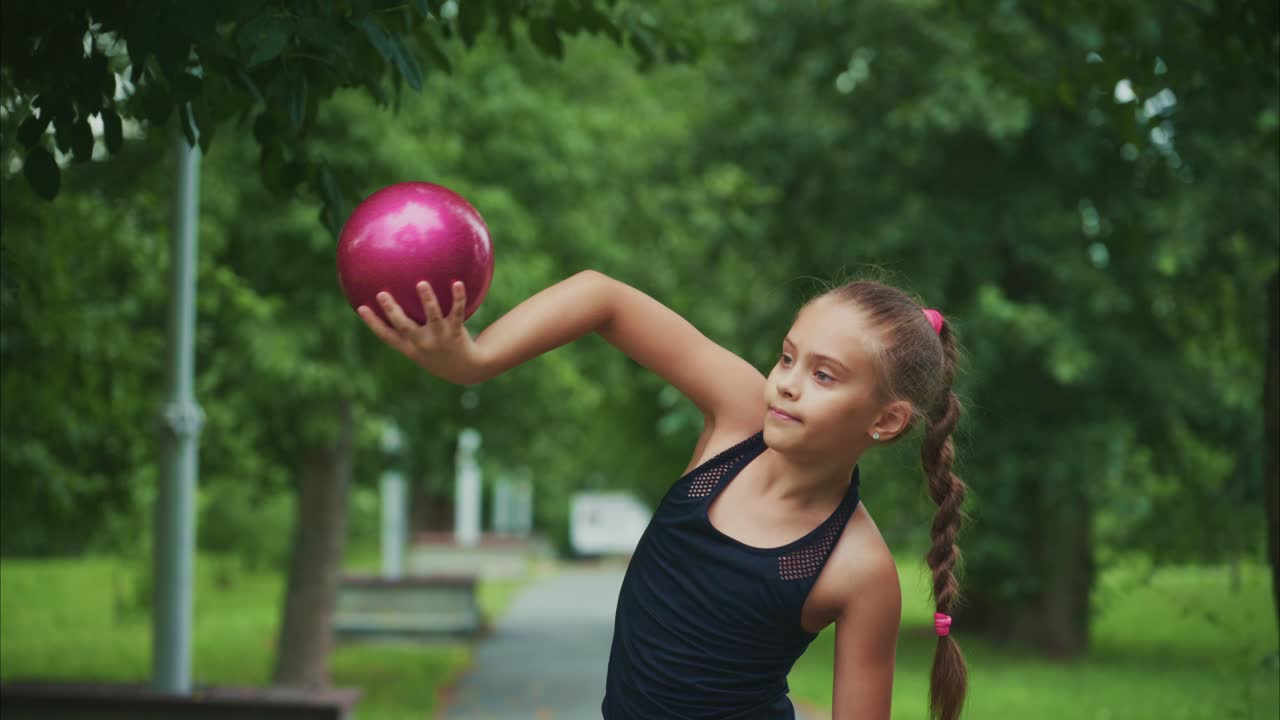 A determined young girl practices her bowling skills in a lush green park, focusing intently on her technique with a pink bowling ball in hand