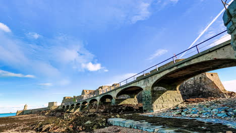 low angle hyperlapse of several people crossing a stone bridge on guernsey coast on sunny day