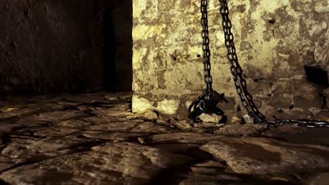 iron chains hanged on stone walls of dungeon inside medieval castle, fear and terror scenery