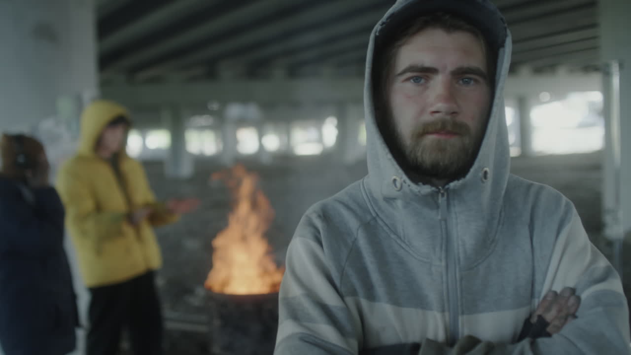 Homeless individuals gathered around a warming fire under an urban bridge