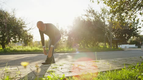 bald man bends down to fix his pants under the sun