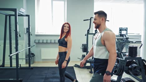 young attractive woman talking to a strong male trainer at the gym. happy athletic couple having a talk while coming into the sports center on the background of modern simulators.
