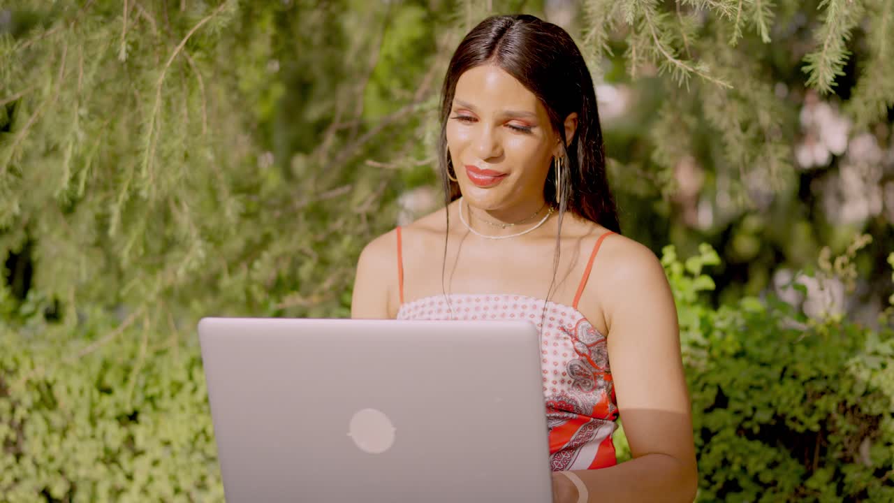Woman smiling while using laptop outdoors in a park