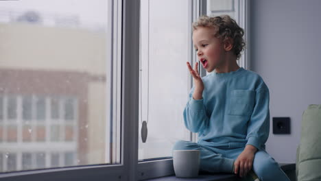 sick child is staying home in winter weekend looking out window admiring snow and trying hot milk