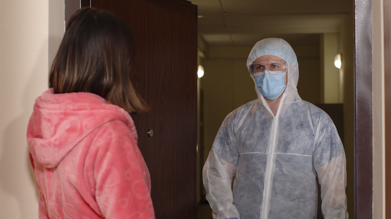 mujer abriendo la puerta de su casa para un médico en traje de peligro biológico médico, vacunación contra el coronavirus