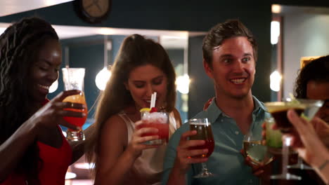 group of young friends meeting for drinks in cocktail bar and making a toast