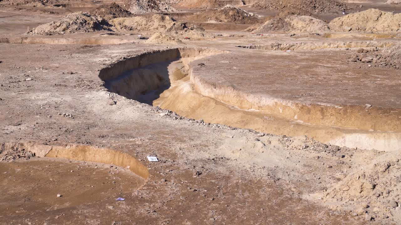 Vista statica di una grande trincea curva scavata nella terra in un sito di scavo archeologico.