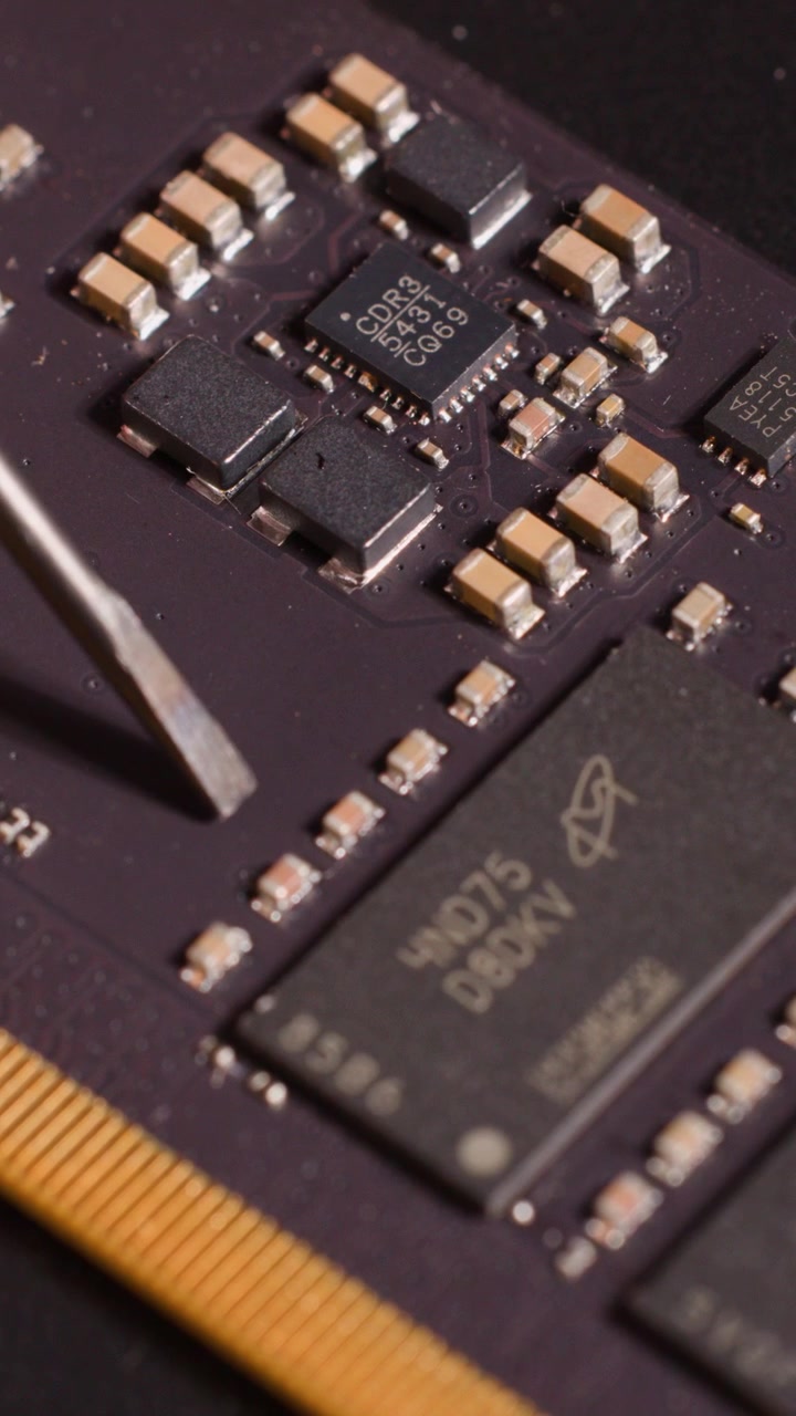 A metal tool inspects components on a computer motherboard in a detailed macro close-up shot
