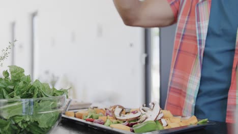 sección media de un hombre biracial preparando comida, vertiendo aceite en las verduras en una cocina soleada, cámara lenta