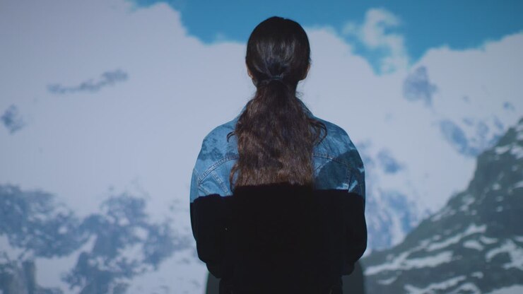 Woman Visiting Immersive Art Exhibition With Images Of Clouds And Mountains Being Projected Onto Wall