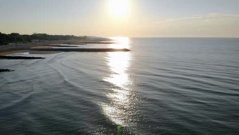 aerial flying over the adriatic sea reflecting the sunset at caorle beach, a coastal town in venice