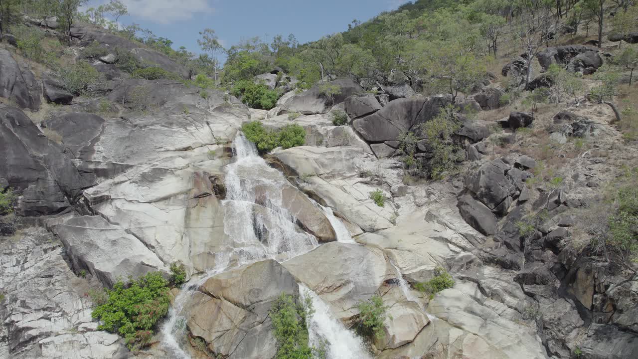 el agua cae en cascada por las cataratas de emerald creek en mareeba, australia durante el día - toma aérea de drones