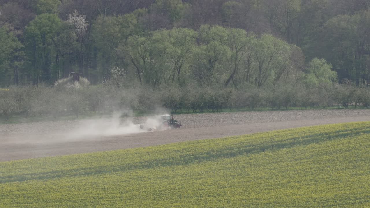Trattore al lavoro in un campo agricolo che solleva una nuvola di polvere, aratura per la raccolta.
