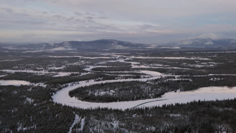 a sweeping aerial survey captures the takhini river as it winds through snowy ibex valley. dense fir forests and a serene winter atmosphere showcase yukon’s raw beauty.