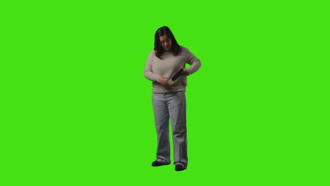 young woman answering call on mobile phone standing against green screen studio background