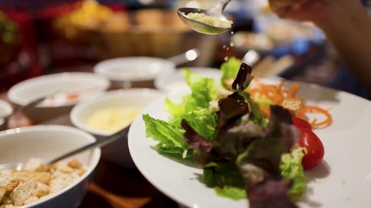 Nærbillede af hænder, der serverer frisk salat med salat, tomater og croutoner ved en international buffet