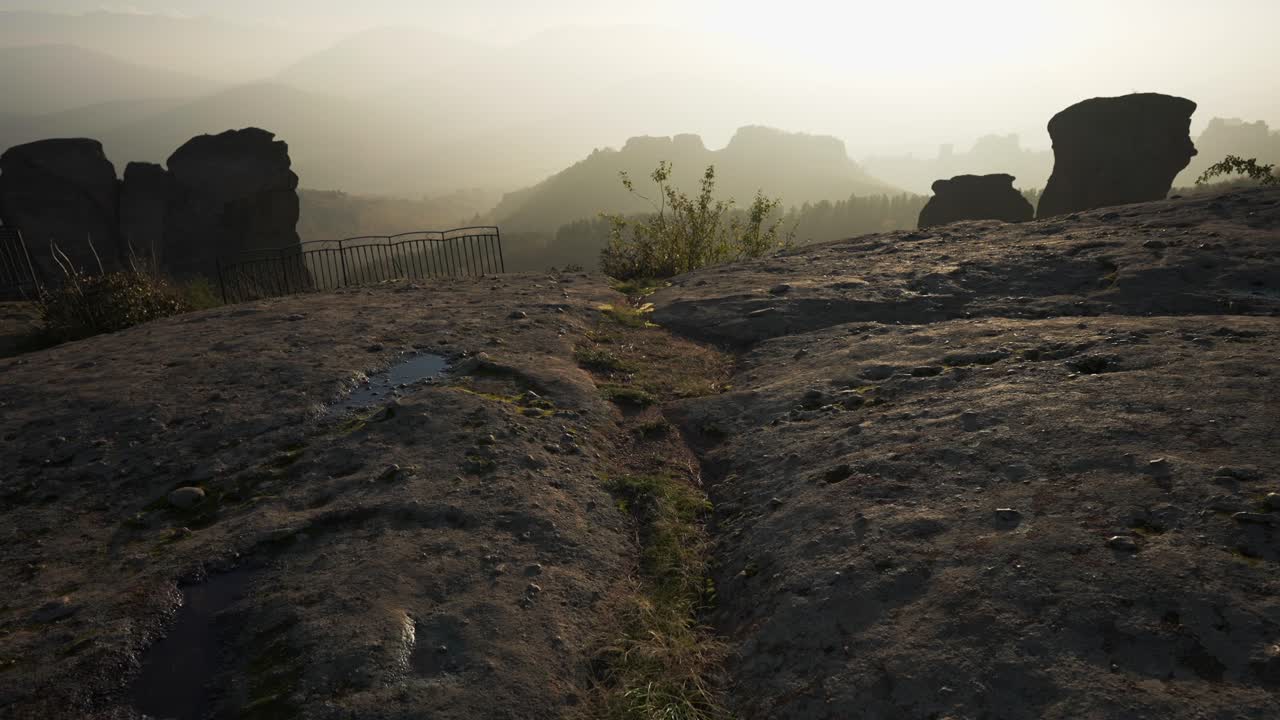 산 꼭대기에서 볼 때, 주변에는 사람이 없고, 태양으로 가득 찬 하늘과 배경에 있는 산을 드러내며, 바위 구조로 둘러싸여 있습니다.