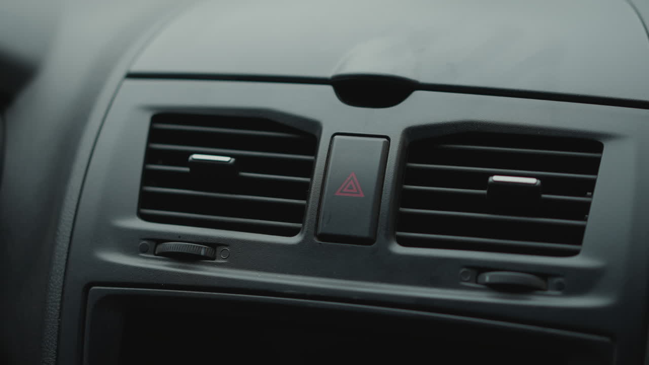 Close up of guy tapping vent button knob on car interior dashboard control detail and finger gesture under ambient cabin lighting highlighting textured slats and panel trim during winter commute