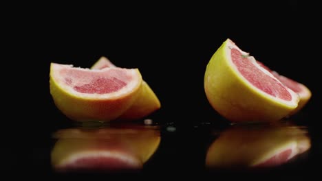 un grapefruit jugoso en rebanadas cayendo sobre un vaso con salpicaduras de agua en cámara lenta sobre un fondo oscuro.