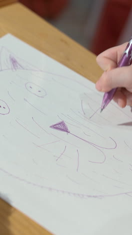 a girl draws a kitten on paper with a pencil. close-up of hands. the child is learning to draw. vertical video