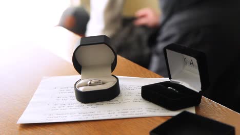 Pan-over-wedding-ring-while-groom-bends-over-in-the-background-to-pick-something-up