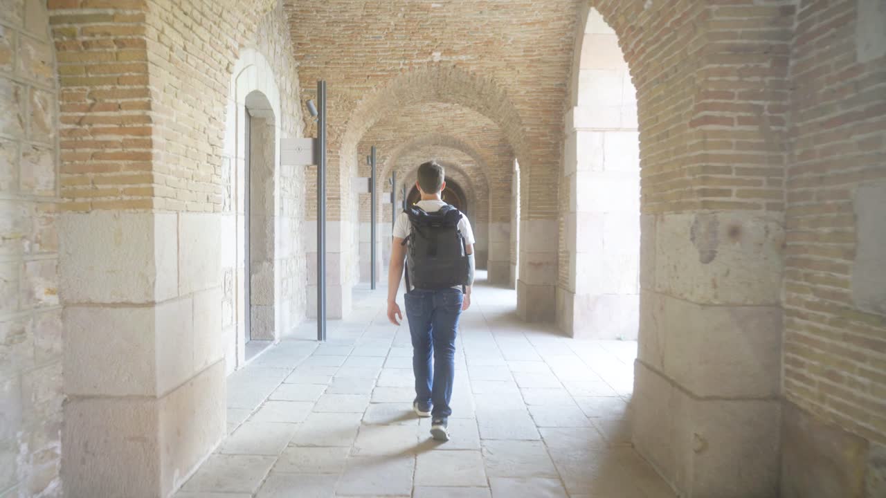 joven con mochila caminando por el pasillo del castillo de montjuic, visitando el museo en un día soleado de vacaciones y visitando la fortaleza militar histórica