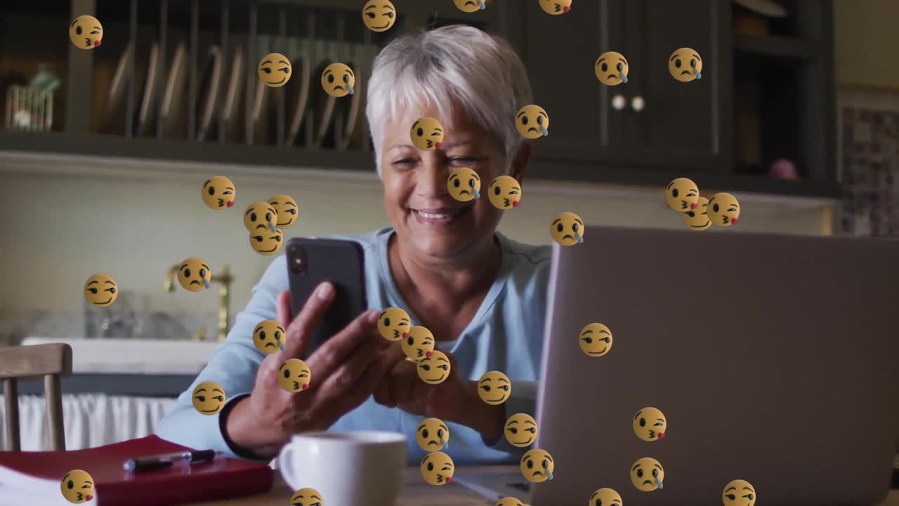 animación de iconos emoji sobre una mujer biracial mayor que usa un teléfono inteligente