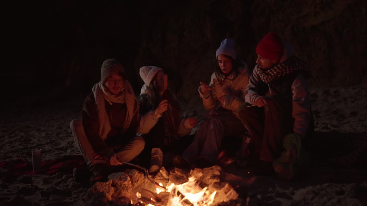 친구 들 이 밤 에 해변 에서 캠프 불 을 즐기고 있다