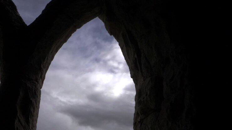 Veduta di cieli cupi e scuri attraverso finestre ad arco di rovine con panoramica ravvicinata.
