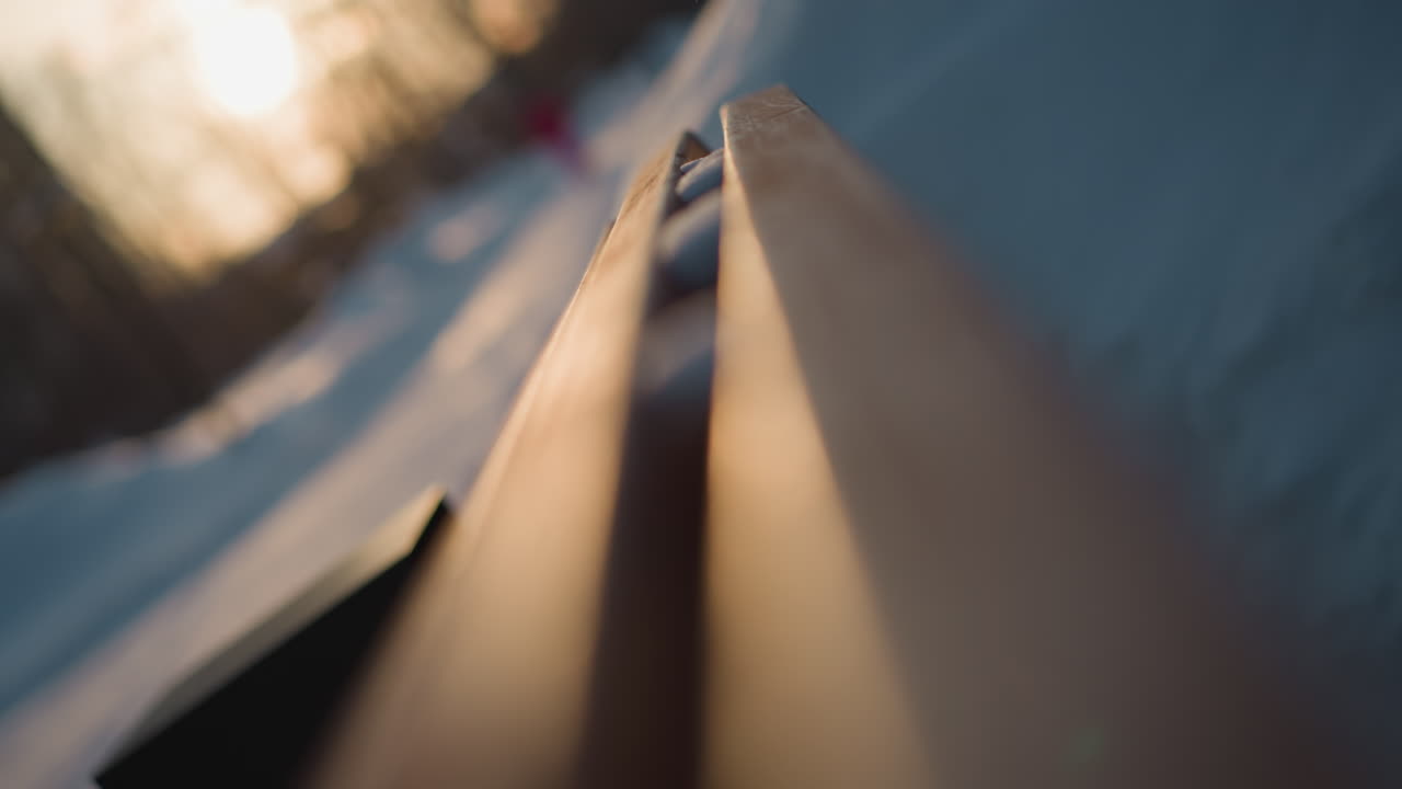 Close up of wooden bench catching golden sunlight glow with soft bokeh background effect in snow covered park during winter season, emphasizing texture and warm tone against icy backdrop