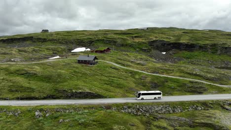 white tourist bus travelling past norway mountain pass during summer - sideways following aerial