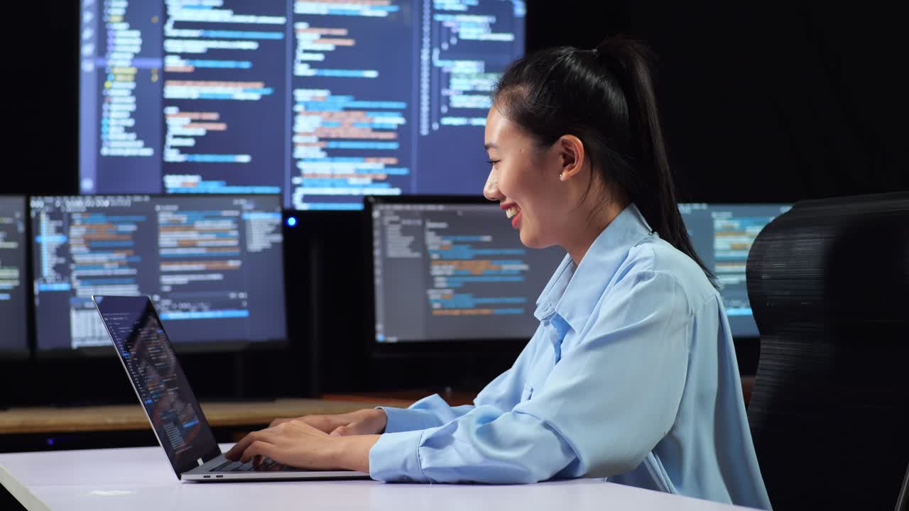 vista lateral de una programadora asiática escribiendo código por una computadora portátil utilizando múltiples monitores que muestran la base de datos en los escritorios de ventana de terminal en la oficina