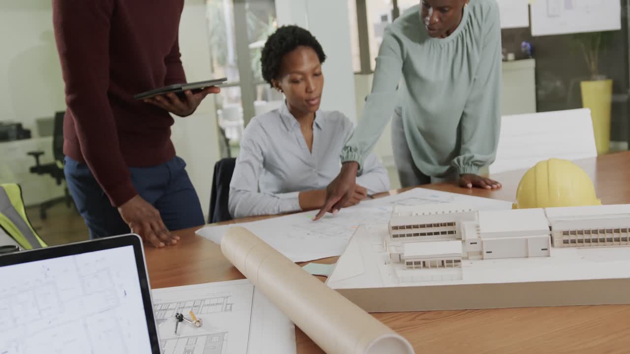 African american male and female architects discussing blueprints in office in slow motion