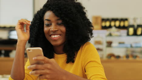 close-up view of african american woman with curly hair texting on the phone sitting at a table in a cafe