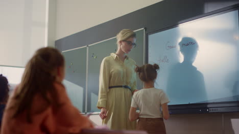 young schoolteacher and schoolgirl standing at smart board in classroom