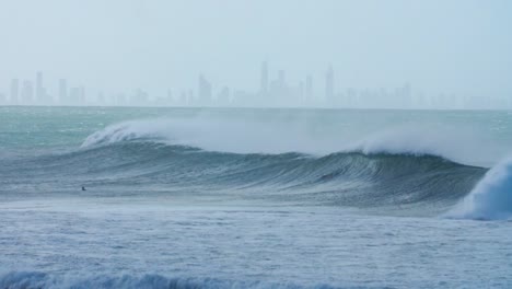 a wave breaking with tall buildings in the background