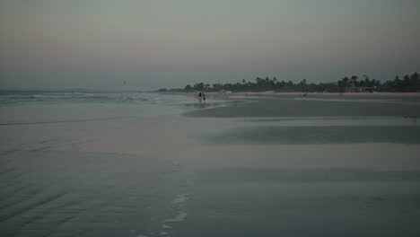 Peaceful-beach-with-small-waves-calmly-crushing-against-the-shore-and-two-people-playing-in-the-water-at-a-distance