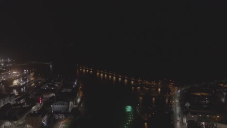 Tilting down, this drone shot from a great height give view to the pier and Galway City surrounding it. The city lights at night illuminate the metropolitan environment