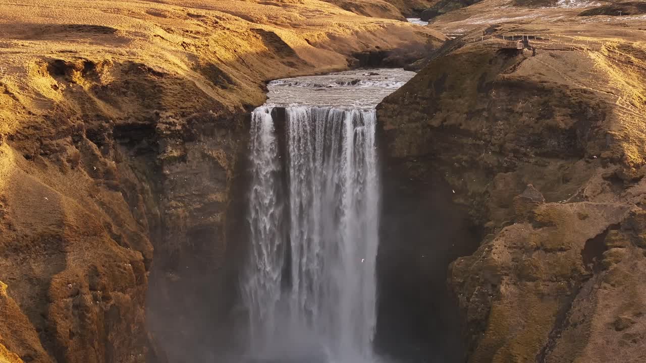 Aerial view of Skógafoss waterfall in Iceland with surrounding golden cliffs and river.