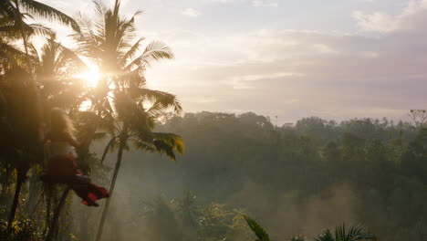 happy woman swinging over jungle at sunrise travel girl enjoying exotic vacation on swing with sun flare shining through palm trees in tropical rainforest holiday lifestyle freedom