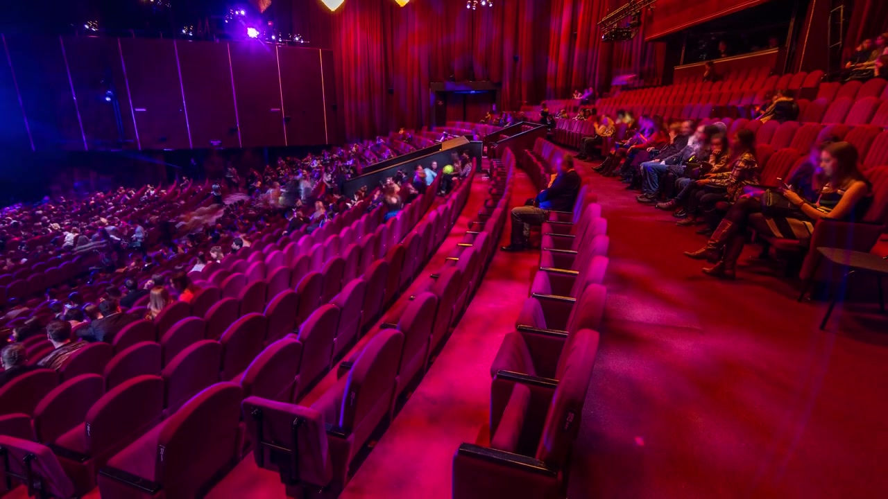 Spectators gather in the auditorium and watch the show in theatre timelapse. Large hall with red armchairs seats. Viewers filling places until turn off the light. View from right side