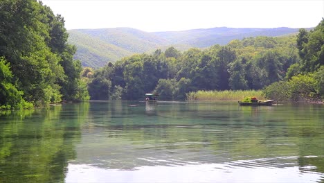 crystal clear pristine transparent water of a natural lake and a small row boat floating far away carrying tourists