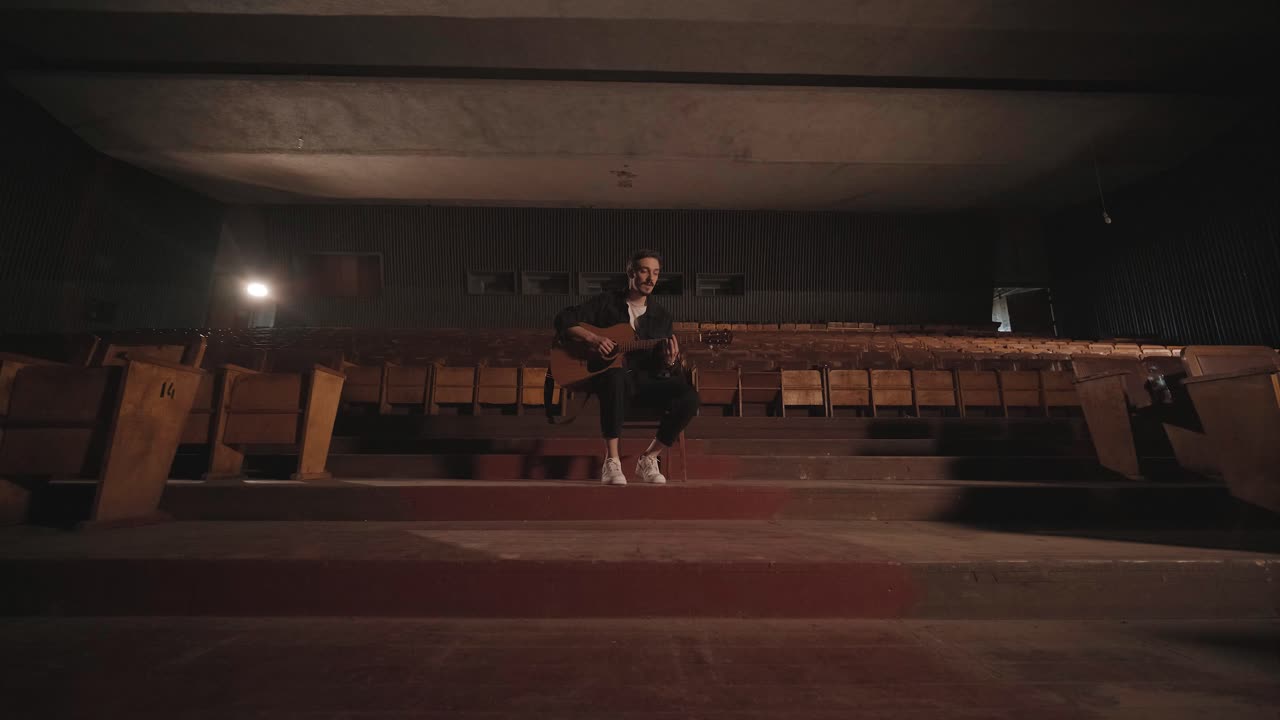 Un bel ragazzo suona una chitarra acustica in un cinema abbandonato. Il musicista canta una canzone e si accompagna con la chitarra