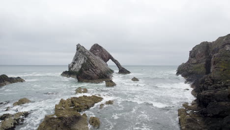 Drohnenantenne-Fliegt-über-Felsigen-Strand-In-Richtung-Riesiger-Felsen-Im-Meer