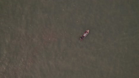 top-down view of a small fishing boat on the water setting the fishing nets
